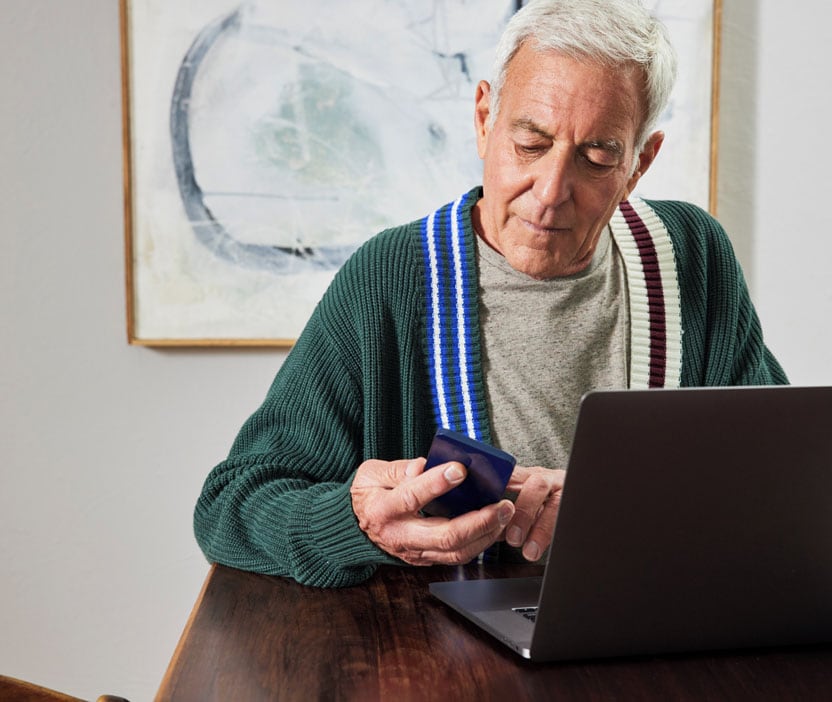 An elderly man using a laptop and phone to remove a fake virus alert, following a step-by-step guide.