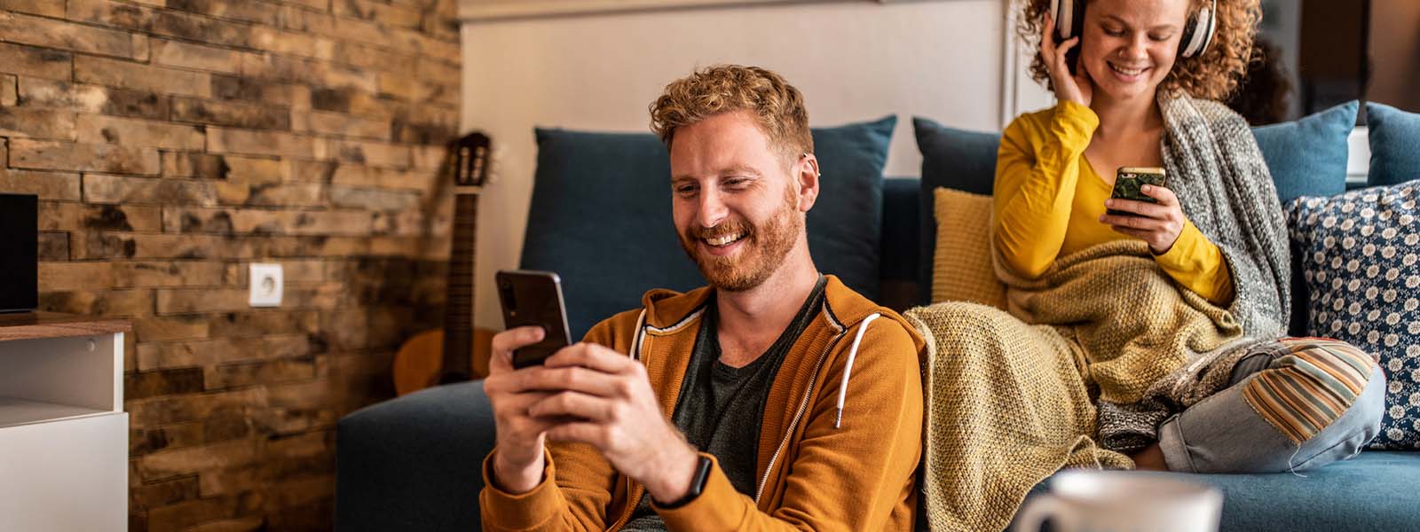 Two friends sit on a couch and use the guest Wi-Fi network to look at their phones.