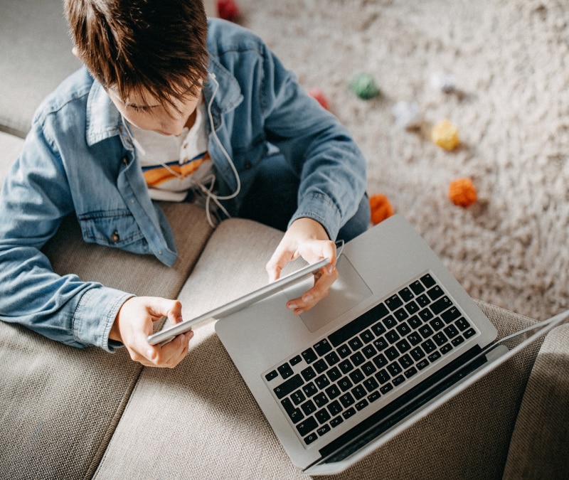 A kid studying using his tablet and laptop.