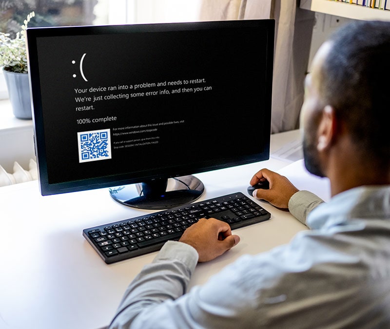 An image of the black screen of death appearing on a man’s desktop computer.