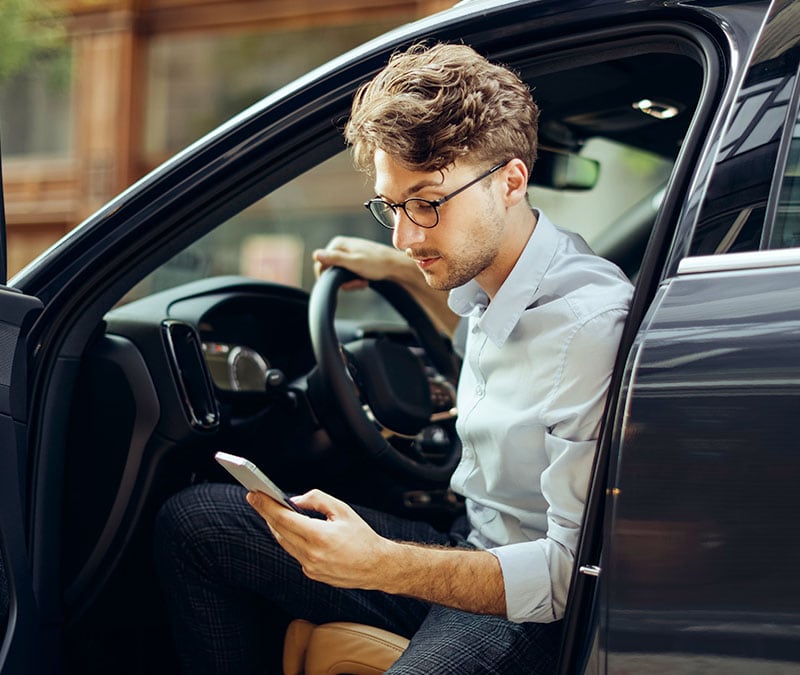 A man looks suspiciously at an E-ZPass scam message as he gets out of his car.