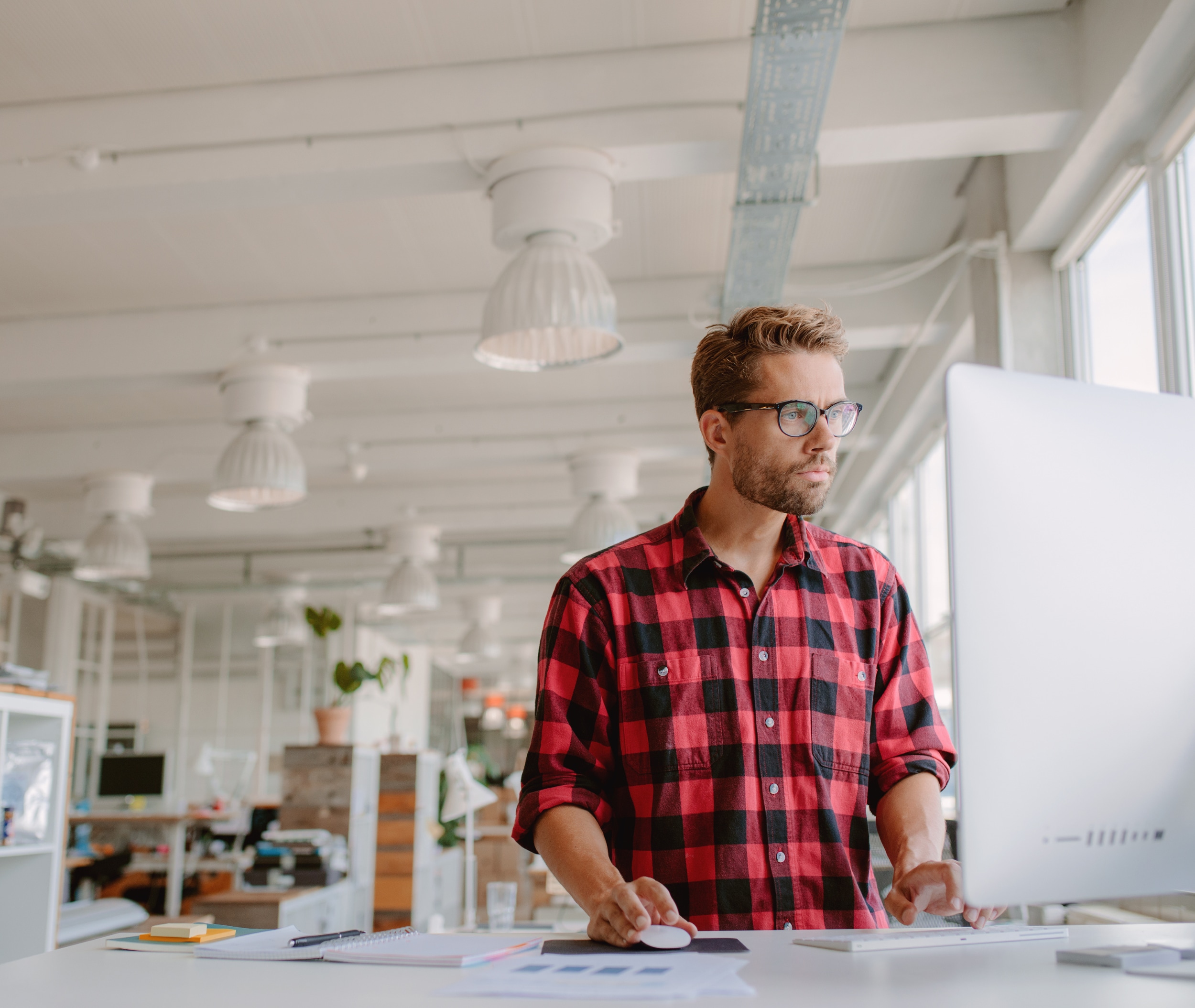 Man standing at desk looking at desktop monitor.