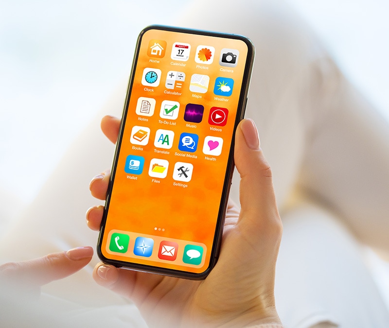 A person holding their iPhone with several apps displayed on the home screen.