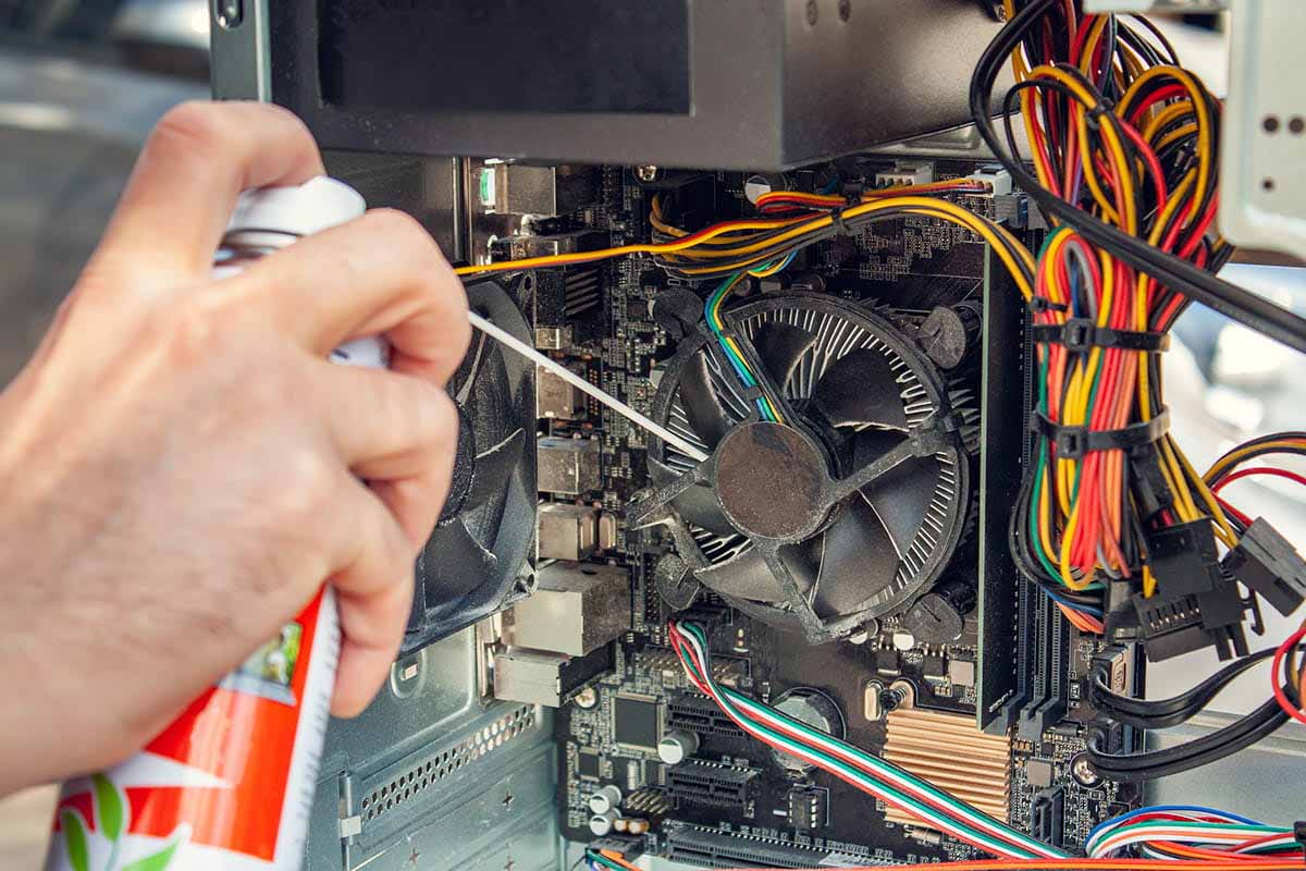 A man sprays compressed air to clean a PC fan.
