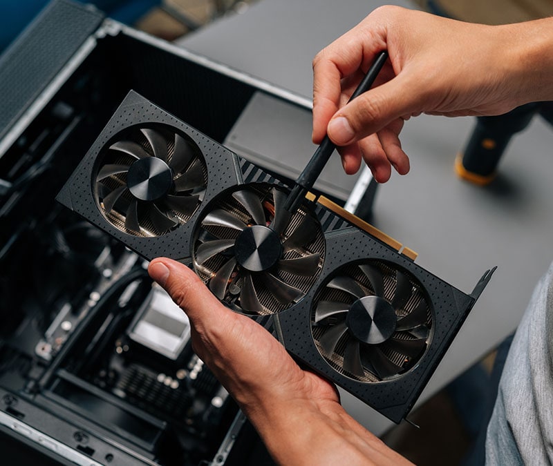A man uses a brush to remove dust from his graphics card fans.
