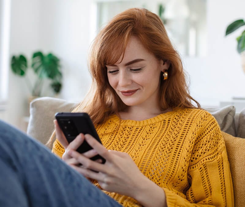 A woman sitting on a sofa clearing the Instagram cache on her iPhone.