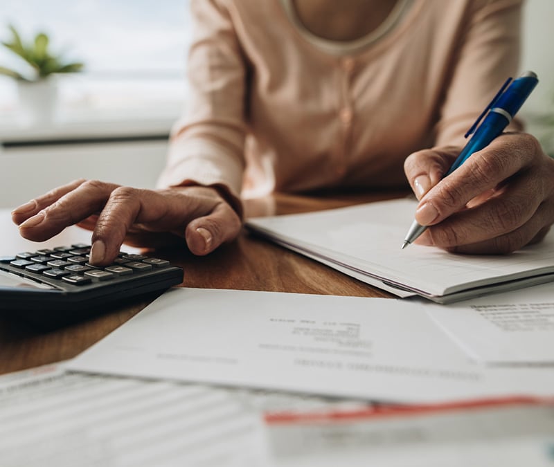 A person sitting a table with paper and a calculator, setting their budget.