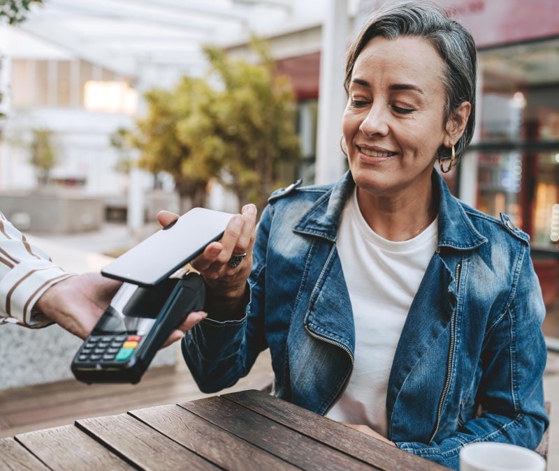 Woman using Apple Pay on her phone at a contactless payment terminal.
