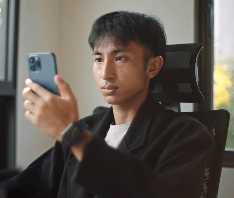 Man holding a smartphone up to his face, potentially using facial recognition to verify his identity for an ID.me account.