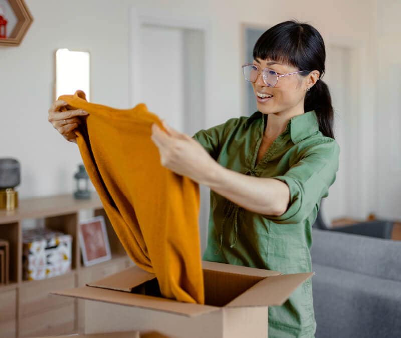 A woman opening a package from Mercari with a yellow sweater.