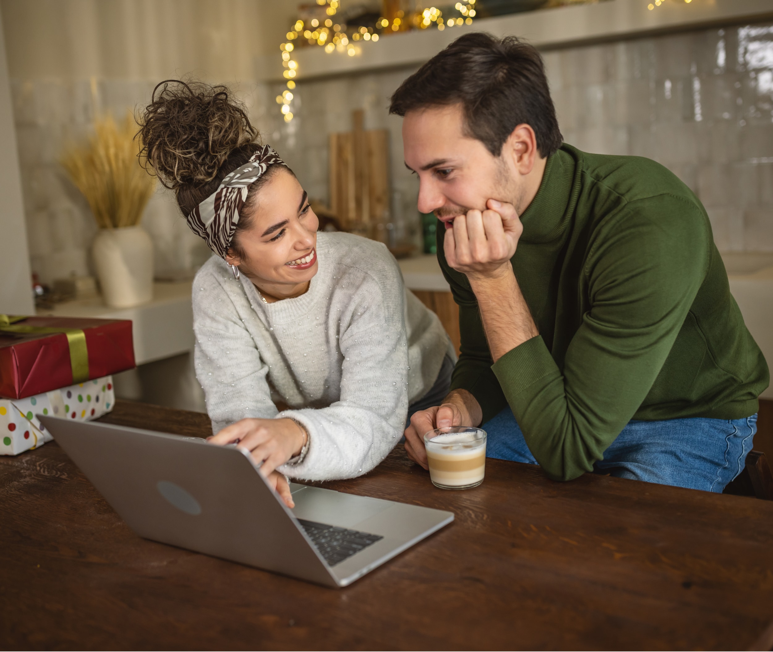 A couple smiling looking at the computer next to wrapped gifts.