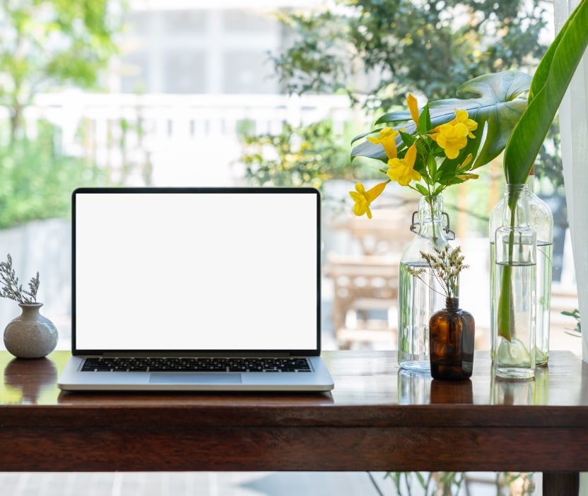 A laptop with a blank screen representing the Phantom Hacker sits on a high table in a coffee shop window with plants around it.