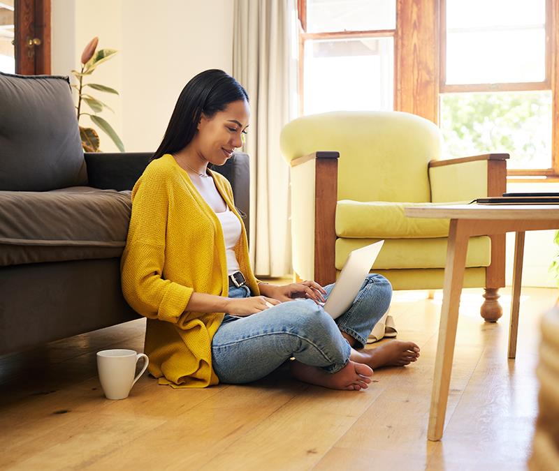 A woman sits on the floor reading her laptop while she discovers Norton ranked highest in the AV-Comparatives quarterly Phishing Comparative test. 