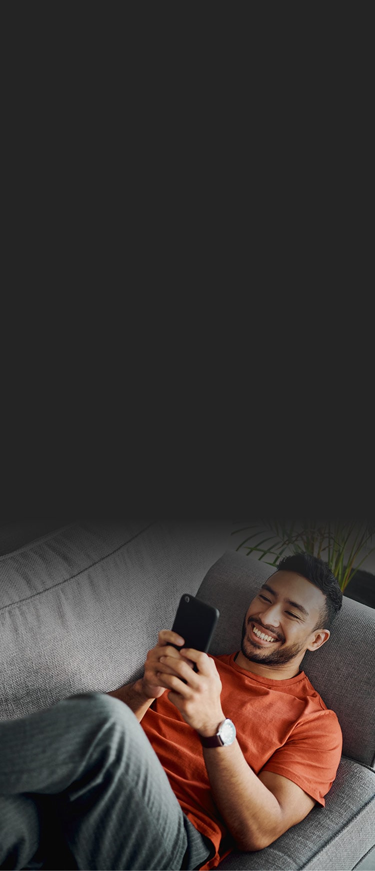 A man lying on a couch and smiling while using a dating app on his phone.