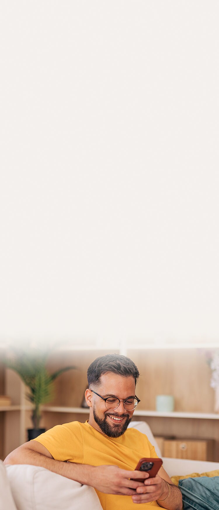 A man in a yellow t-shirt smiling at his phone. 