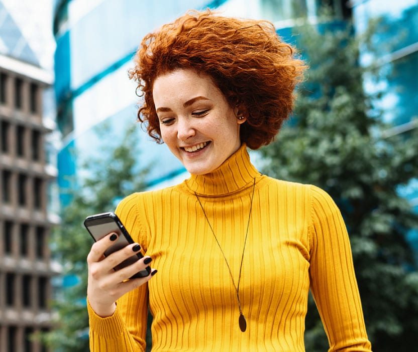 A woman in a yellow turtleneck using her phone to learn about secure messaging.