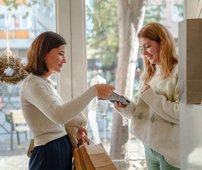 A customer taps her card on a payment device held by a small business owner.