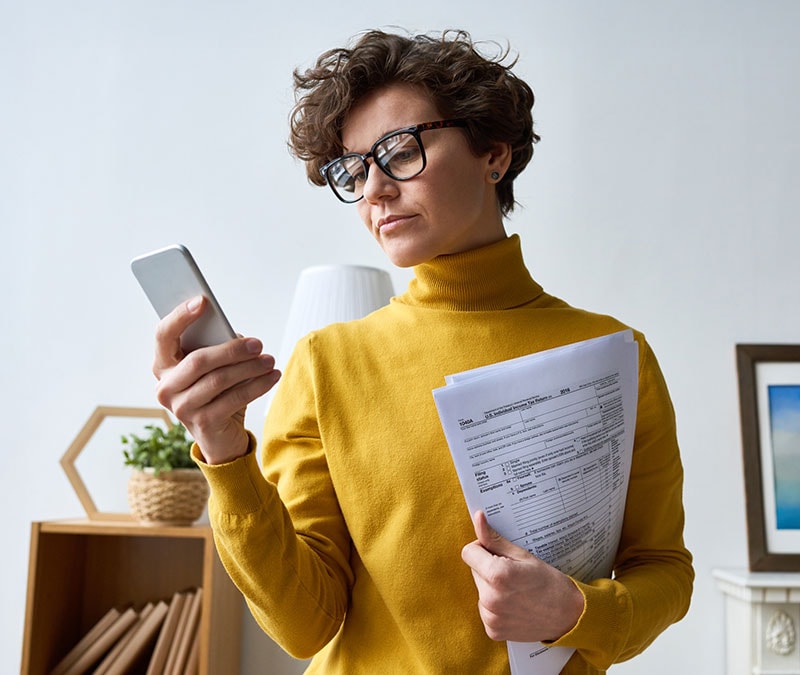 A woman in a yellow turtleneck with her tax return in hand.
