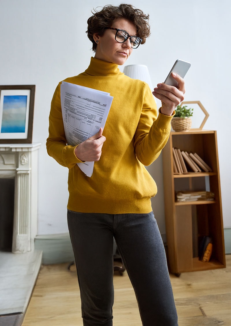 A woman in a yellow turtleneck with her tax return in hand.