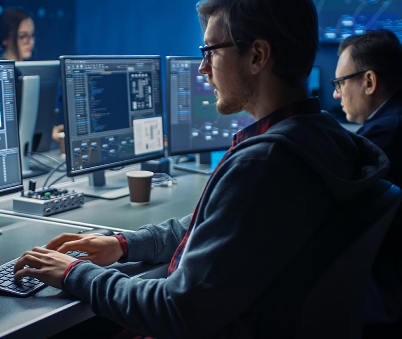 A hacker sitting in a dark room with code displayed on his computer.