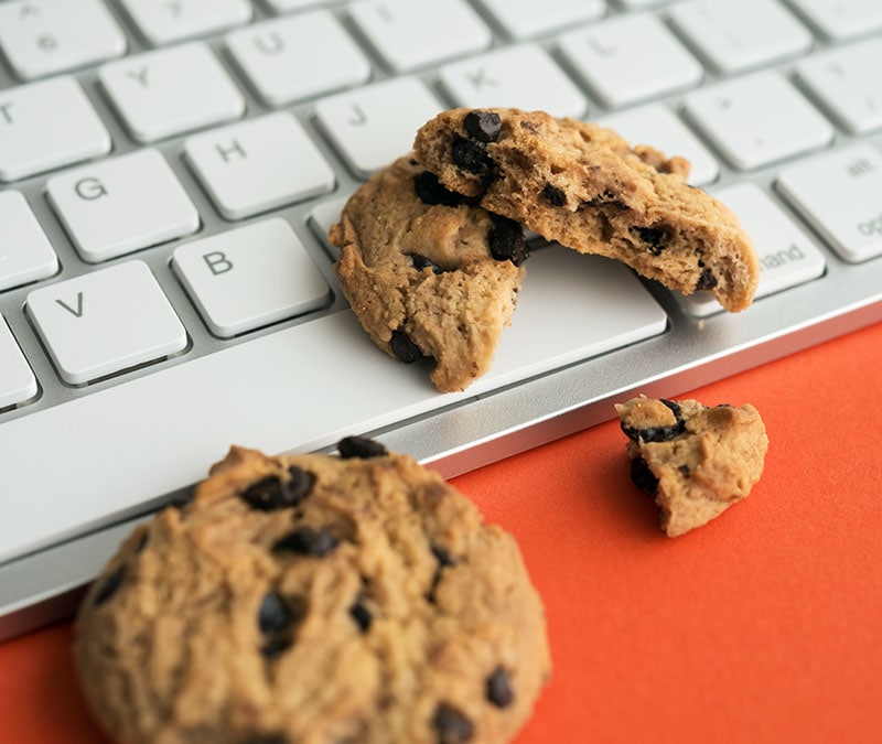 Image of baked cookies on a computer’s keyboard, one piece broken off to represent the trail of tracking cookies.
