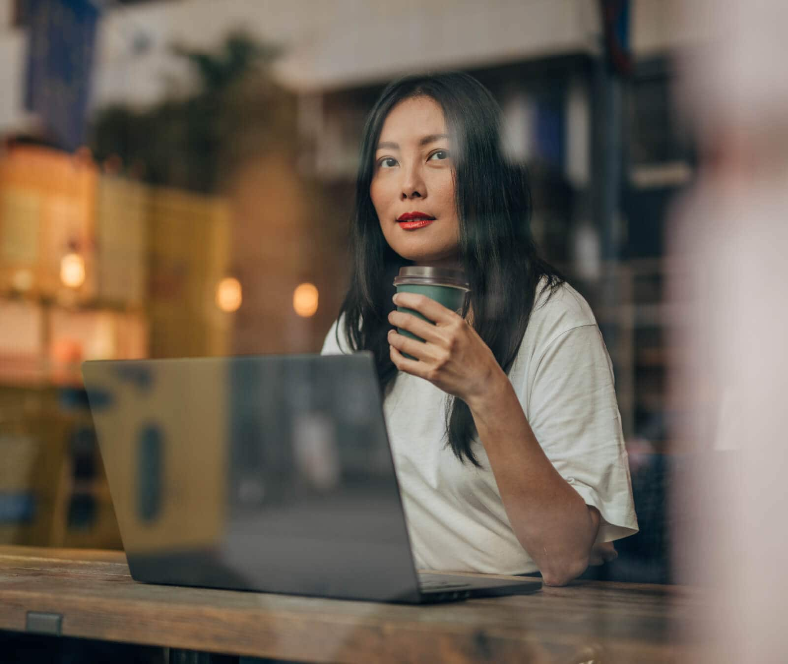 Woman working on her laptop at a coffee shop looking out the window.