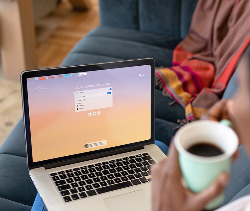 A person using an agentic browser on their laptop, cup of coffee in hand.