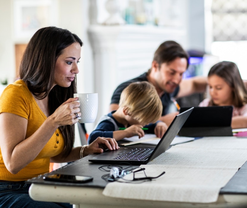 A mom sits at her laptop, learning about IRS IP PINs in 2024, with her family in the background.