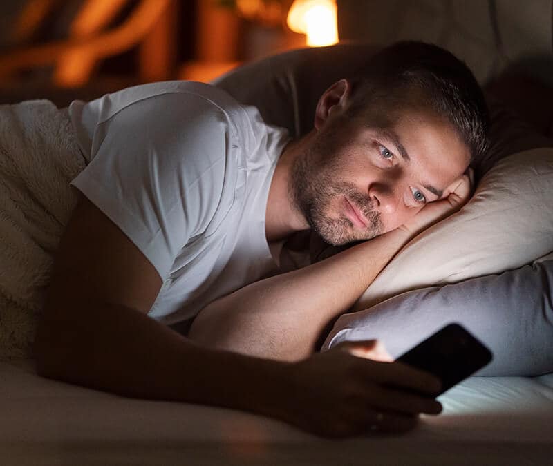 A man lies in bed while using a smartphone.