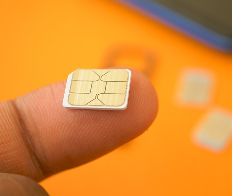 Close-up of a finger holding a small SIM card against a vibrant orange background.