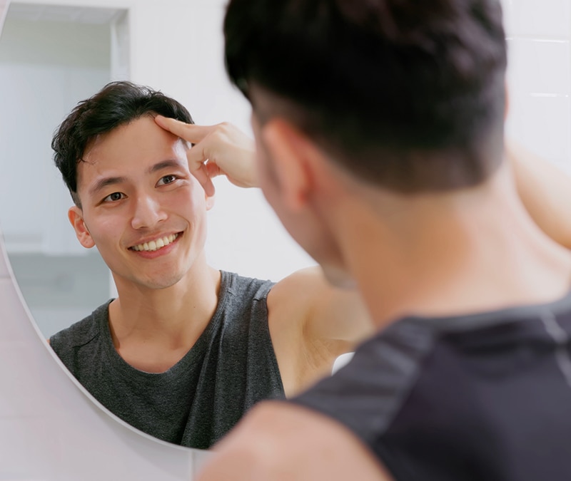 A man looking in the mirror as an example of social engineering, a malicious tactic used to gain access to confidential information.