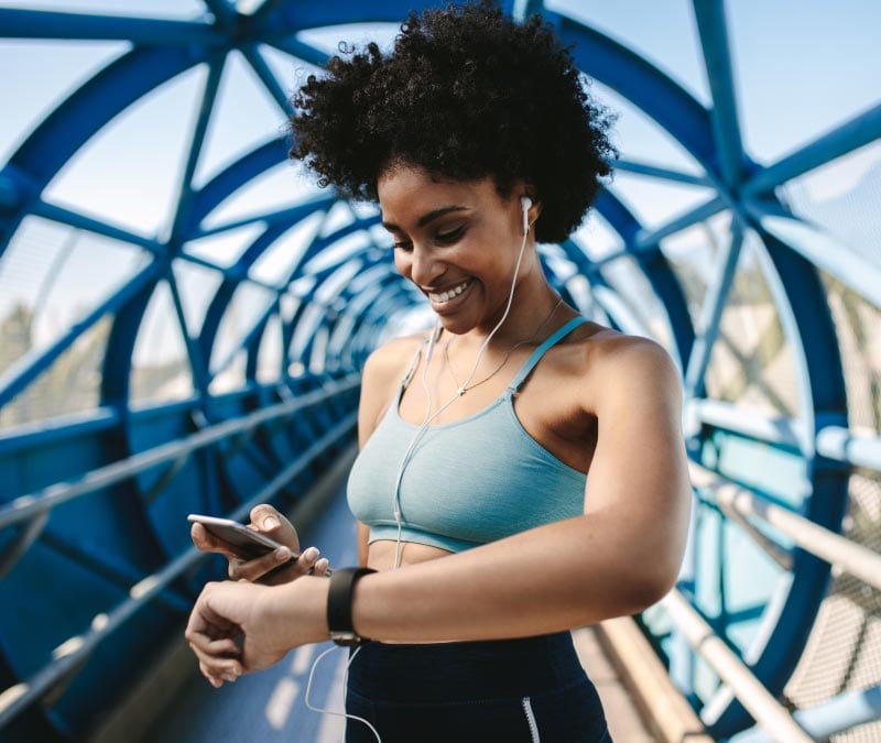 A woman uses two IoT devices, a smartwatch and smartphone, to monitor her health metrics on a run.