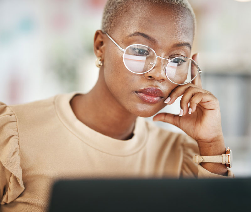 A woman with glasses looks suspiciously at her laptop screen, potentially because her email was hacked.