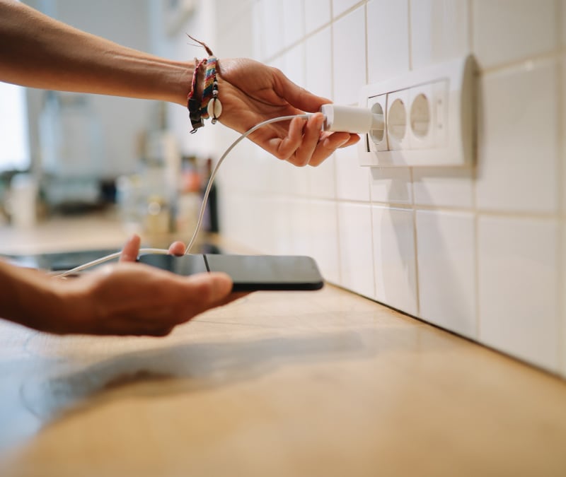 A person plugging in their smartphone to charge because their battery is draining so fast.