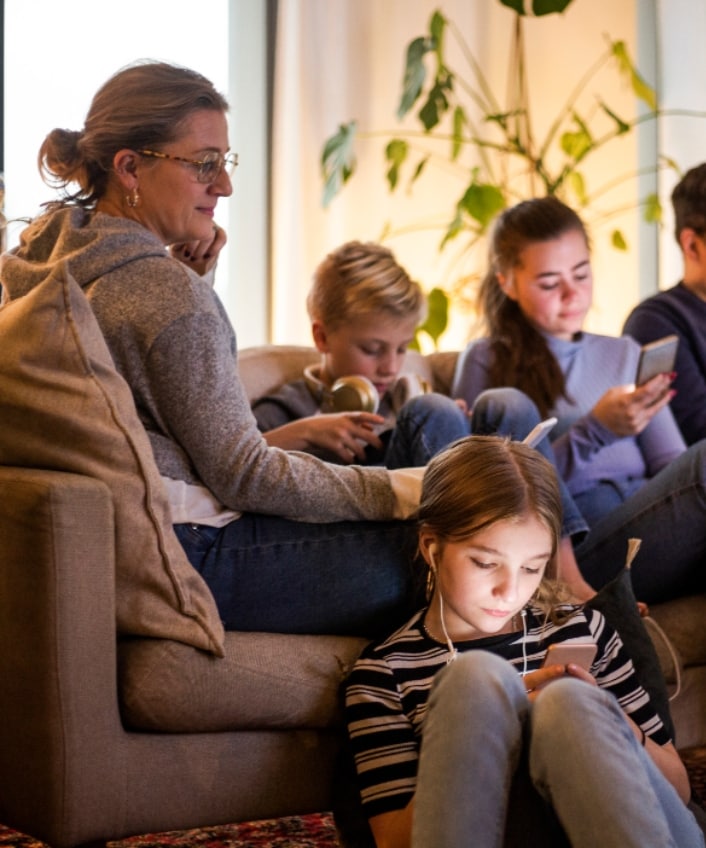 A family of four sits on the couch, each watching online streaming on their own device.