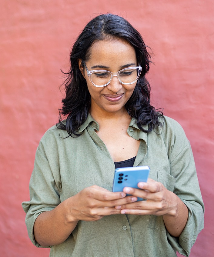 A woman wearing glasses focusedly looks at her phone screen.