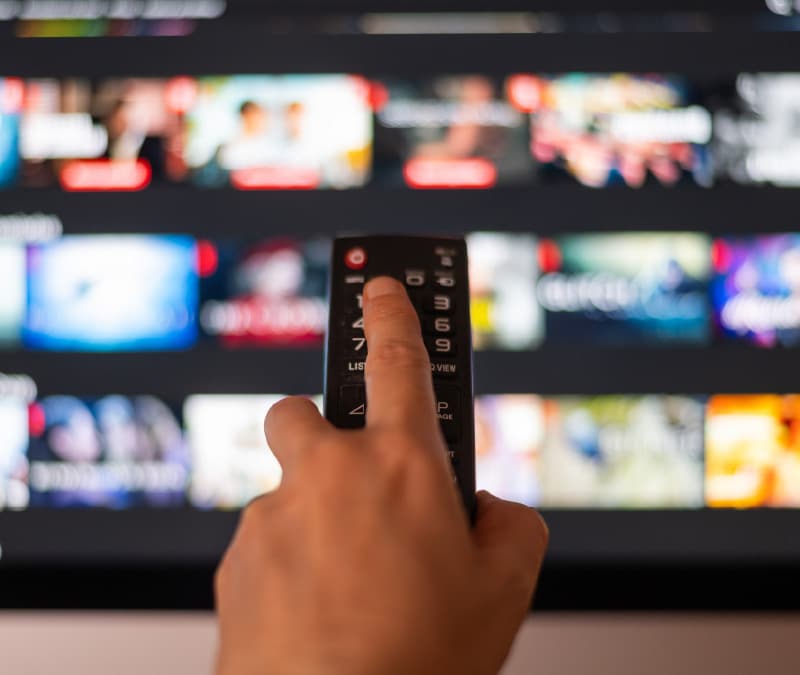 A hand holding a TV remote controller pointing at a TV trying to cancel a streaming subscription.