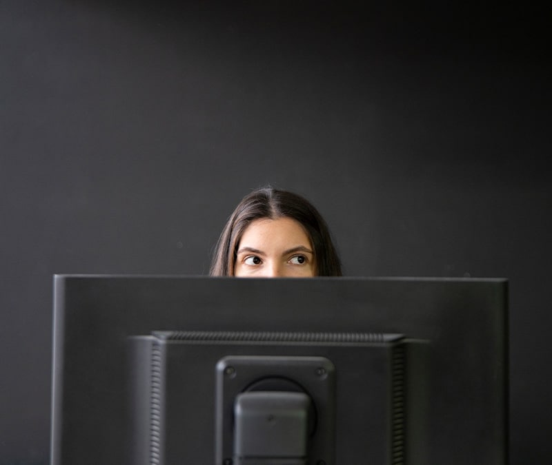 A woman hides behind a computer screen.