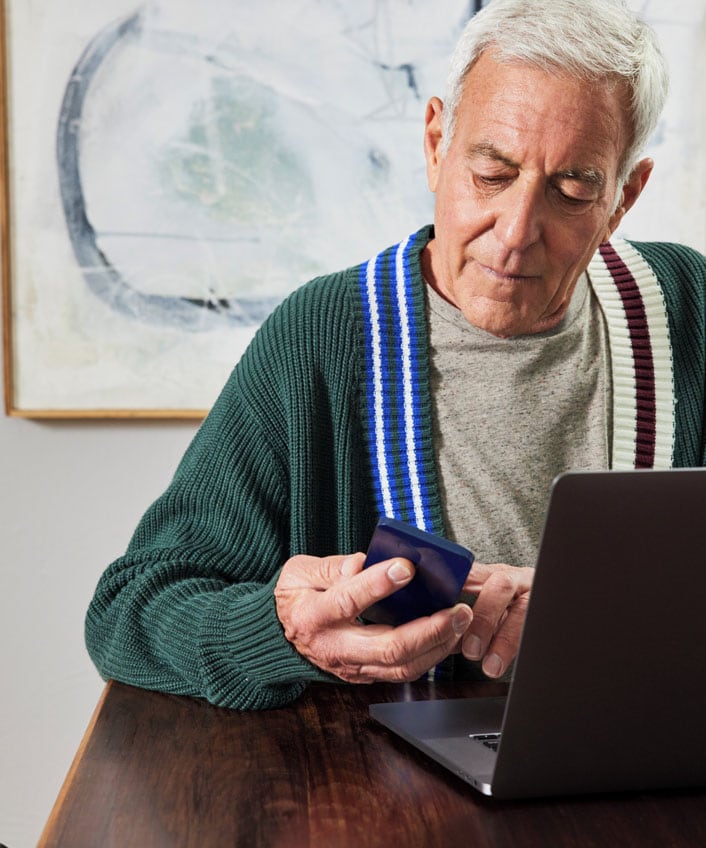 An elderly man using a laptop and phone to remove a fake virus alert, following a step-by-step guide.
