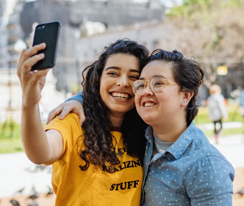 Two friends taking a selfie and smiling, knowing they have Norton to help prevent an Instagram hack.
