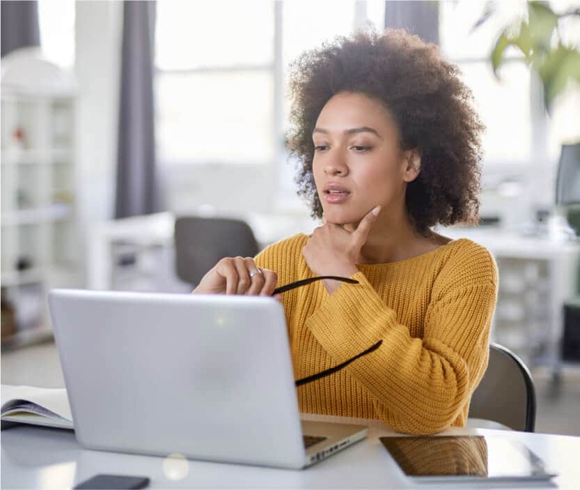 A woman wears a  yellow sweater looking at her computer and determining whether or not she is a victim of a LinkedIn scam.