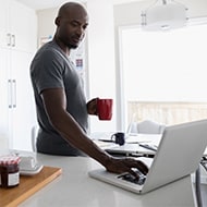 A man using laptop with cup of coffee in hand, preparing to clean his computer.