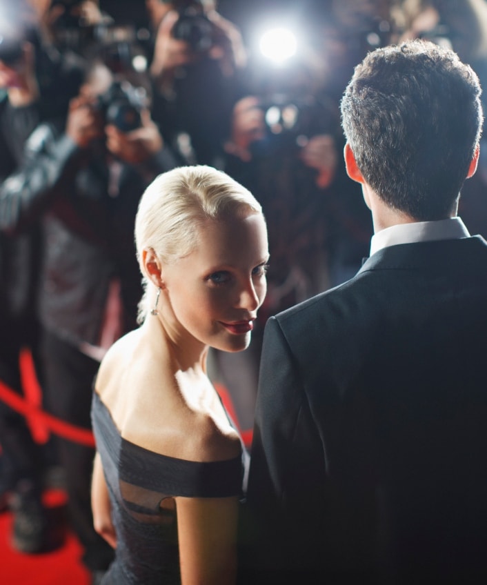 A blonde woman on a red carpet looks back over her shoulder at the camera.