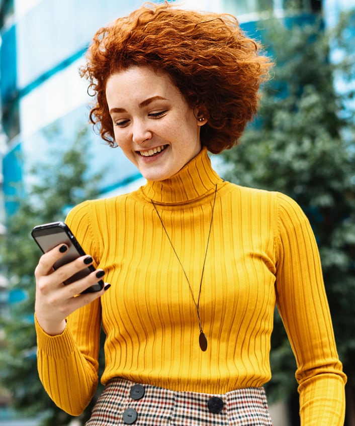 A woman in a yellow turtleneck using her phone to learn about secure messaging.