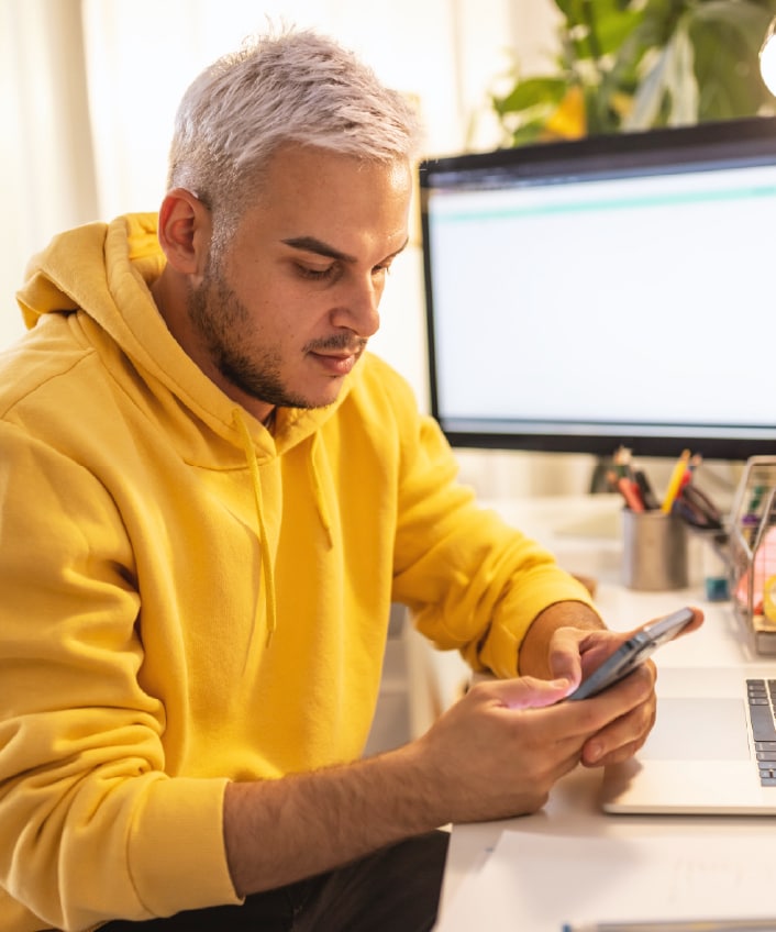 A man in a yellow sweatshirt looking at his phone learning about social media scams.