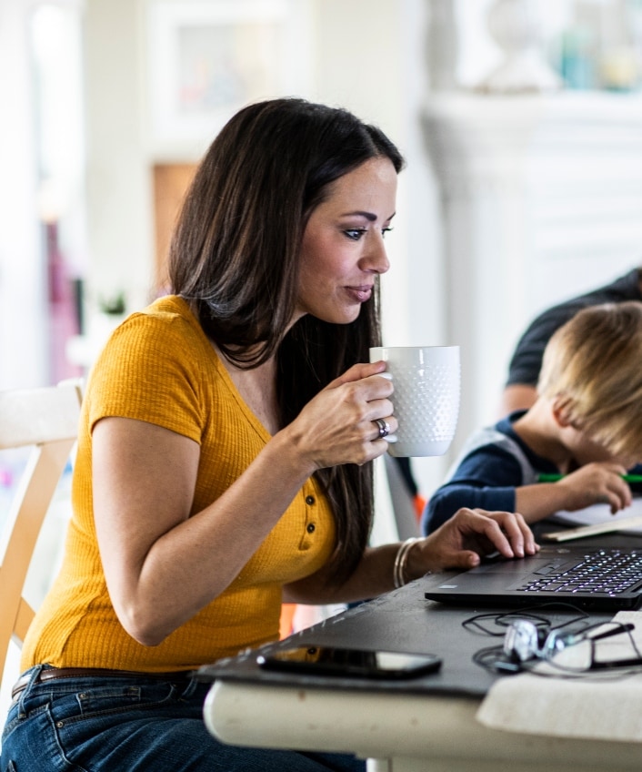 A mom sits at her laptop, learning about IRS IP PINs in 2024, with her family in the background.