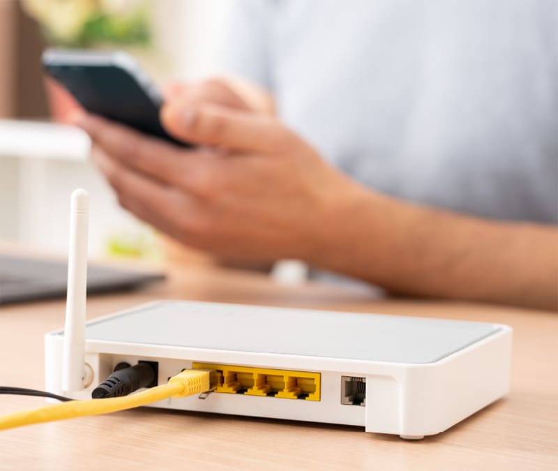 A person using their phone next to a Wi-Fi router trying to increase internet speed.