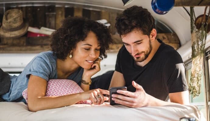 man and woman on bed looking at cell phone launching Norton 360 with LifeLock Advantage.