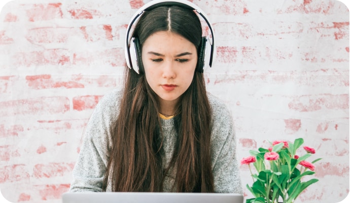 A yong girl with headphones on looking at a Laptop.