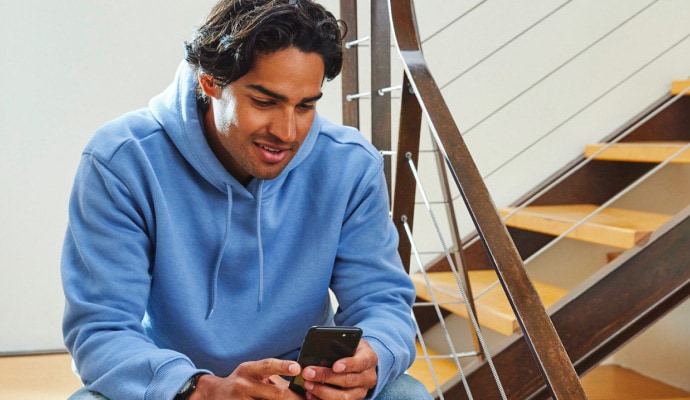 Man in blue hoodie sitting on stairs and smiling at phone
